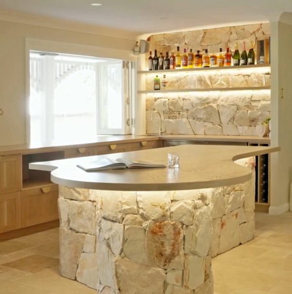 Entertainment kitchen area that seamlessly blends Sydney Sandstone, the warmth of American Oak, and the exquisite touch of brass drawer handles.